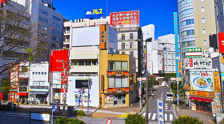 Veduta stradale urbana vicino alla stazione di Gotanda a Tokyo con numerosi cartelloni pubblicitari e edifici moderni.