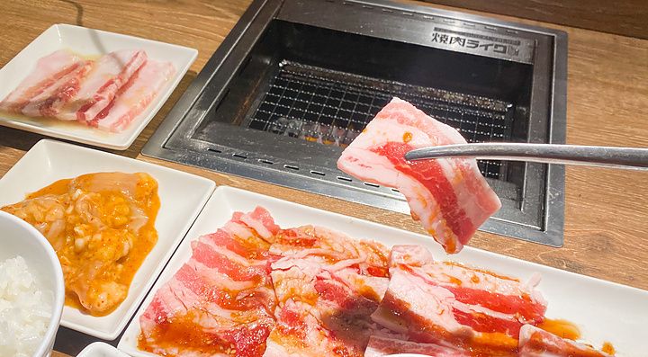 Una fetta di carne cruda sollevata con le bacchette sopra una griglia presso il ristorante Yakiniku Like.