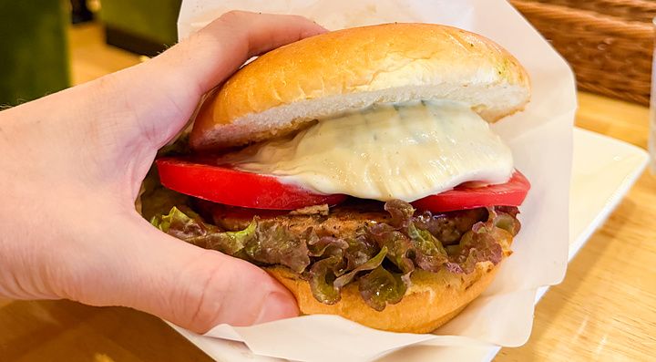 Una mano tiene un hamburger vegano farcito con pomodoro e lattuga servito nel ristorante Komeda Is a Ginza.
