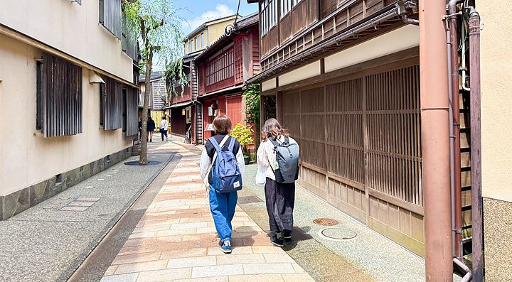 Due persone con zaino percorrono una strada lastricata nel quartiere tradizionale di Higashi Chaya a Kanazawa.