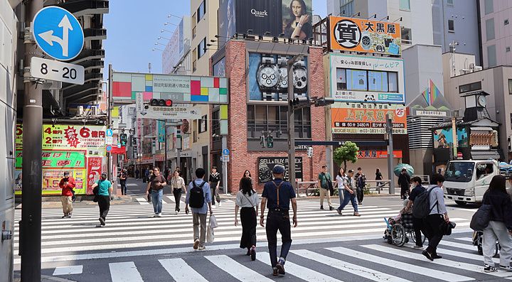 Persone che camminano sulle strisce pedonali vicino alla stazione di Okachimachi a Tokyo in una giornata di sole.