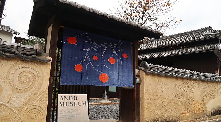 Ingresso dell'Ando Museum a Naoshima con cancello, noren blu decorato e parete in stucco lavorato.