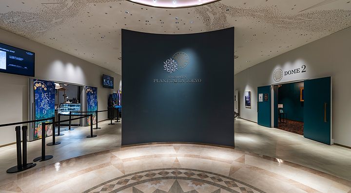 Ingresso del Planetaria Tokyo con pavimentazione in marmo decorato, parete curva centrale e ingressi laterali.