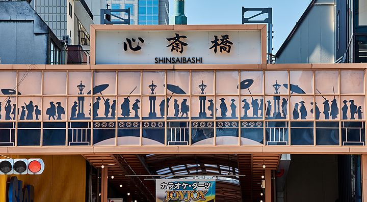 Insegna decorata dell'ingresso di Shinsaibashi a Osaka con silhouette di persone e caratteri giapponesi.