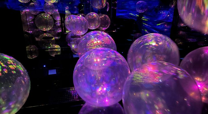 Installazione artistica con sfere traslucide illuminate da luci colorate in una sala oscura a Kyoto.