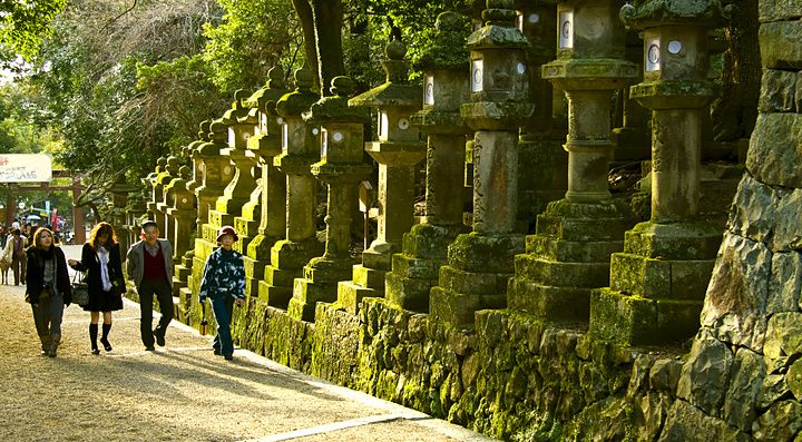 Turisti camminano accanto a lanterne di pietra con muschio al santuario Kasuga Taisha, Nara.