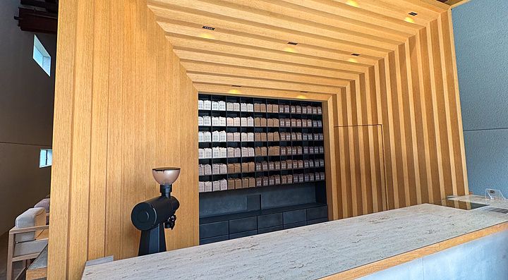Veduta interna di Koffee Mameya Kakeru a Tokyo con bancone in pietra e una parete espositiva in legno per il caffè.