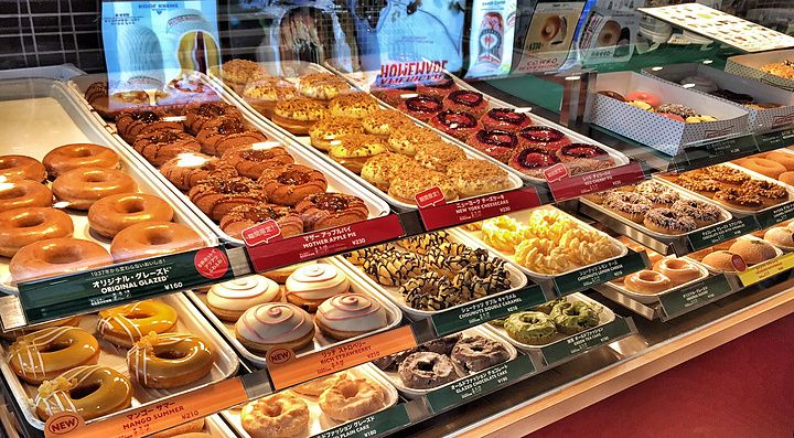 Espositore di ciambelle assortite all'interno di un negozio Krispy Kreme a Tokyo con una persona visibile.