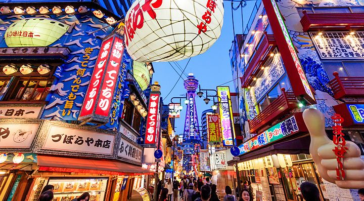 Strada animata di Shinsekai a Osaka con una grande lanterna a forma di pesce palla e la torre Tsutenkaku sullo sfondo.