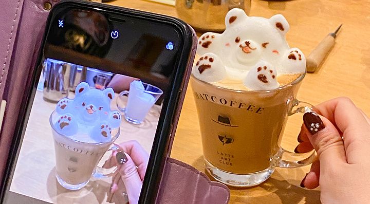 Una persona fotografa con lo smartphone una tazza di cappuccino con latte art a forma di orso presso Hatcoffee ad Asakusa.