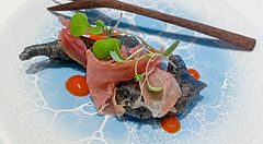 Un antipasto al Koji Shimomura composto da gnocco fritto con calamaro e prosciutto crudo italiano su un piatto azzurro.