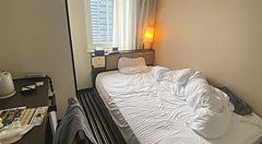 Interno di una camera compatta presso l'Apa Hotel a Shinjuku con letto singolo disfatto e finestra urbana.