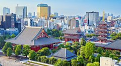 Veduta panoramica del tempio Senso-ji ad Asakusa con le sue pagode rosse circondate da alberi e grattacieli sullo sfondo.