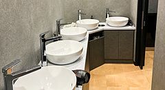 Bagno in comune con lavandini moderni, specchi rotondi e pareti grigie.