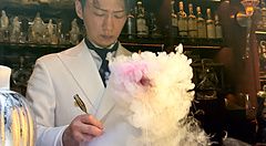 Un barista in divisa bianca prepara un cocktail fumante dietro il bancone del Bar Centifolia a Tokyo.