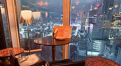 Tavoli e sedie di Cafe Legato a Shibuya posizionati accanto a una grande vetrata che affaccia sulla città piovosa.