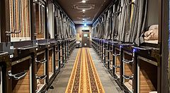 Corridoio interno del capsule hotel Anshin Oyado a Shinjuku con due file di capsule letto e moquette decorata.