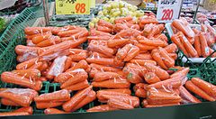 Carote confezionate su scaffali in un supermercato giapponese con cartelli dei prezzi.