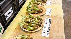 Rizomi di wasabi fresco in vendita su cestini di vimini con cartellini dei prezzi a Daio Wasabi Farm, Nagano.