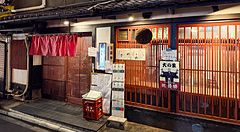 L'esterno di Gion Yuki a Kyoto presenta una facciata in legno scuro con infissi a listelli rossi e insegne informative.