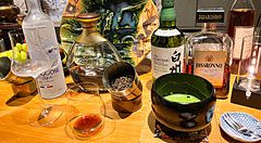 Bottiglie di alcolici, una ciotola di matcha e un piatto decorativo sul bancone in legno del Mixology Salon a Ginza.