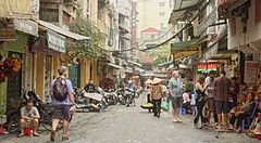 Strada di Hanoi con pedoni, motorini e negozi animati.