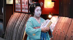 Una giovane maiko in kimono azzurro cammina in un vicolo tradizionale di Kyoto.