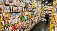 Una persona accovacciata tra gli scaffali pieni di manga all'interno del negozio Mandarake a Tokyo.