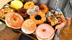 Marco Togni sorridente tiene un vassoio pieno di ciambelle presso a Mister Donuts.