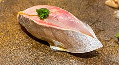 Un nigiri di aji con guarnizione verde servito su un piatto in ceramica scura da Sushi Takeuchi a Tokyo.