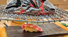 Un nigiri di otoro scaldato coi carboni ardenti da Sushi Tou con uno chef che maneggia la brace su una griglia.
