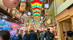 Veduta interna del vivace Nishiki Market a Kyoto con persone che camminano sotto un soffitto decorato da pannelli colorati.