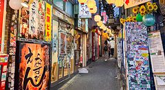 Ingresso del vicolo Omoide Yokocho a Shinjuku, caratterizzato da un'insegna verde, lanterne decorative e pareti piene di a...