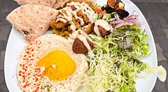 Un piatto misto vegano a Falafel Sababa composto da hummus, falafel, insalata e pane pita tenuto in mano a Namba, Osaka.