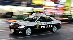 Volante della polizia giapponese in transito notturno lungo una strada urbana in Giappone.