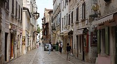 Strada del centro storico con negozi a Porec, Croazia, persone passeggiano.