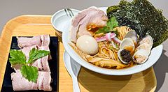 Una ciotola di ramen con vongole e carne servita su un vassoio di legno presso il ristorante Mugi to Olive a Tokyo.