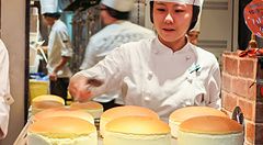 Una pasticcera in divisa lavora nel negozio Rikuro’s ad Osaka, marchiando a fuoco diverse cheesecake rotonde.