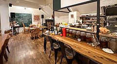 Veduta dell'interno del ristorante a Ristorante Momose Shokudo con bancone in legno, tavoli e lavagna con menu.