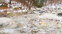 Veduta invernale di un ruscello termale nel Sainokawara Park, tra rocce, vapore e neve.