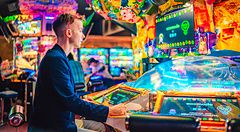 Persona gioca in una sala giochi giapponese, circondato da luci colorate.