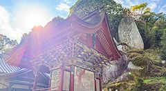 Veduta della struttura in legno rosso del Santuario Iwagami sull'isola di Awaji con il gigantesco masso sacro retrostante.