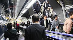 Molte persone si spostano sulle scale mobili all'interno di una moderna struttura tubolare di transito in Giappone.