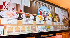 Uno schermo per ordinare a Sushiro con immagini di piatti di sushi e dessert selezionabili tramite interfaccia touch.