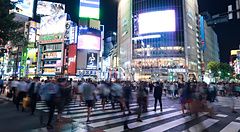 Veduta notturna dell'incrocio di Shibuya a Tokyo con una folla di persone in movimento che attraversano la strada.