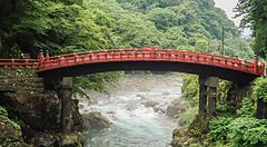 Il ponte Shinkyo a Nikko sopra un fiume circondato da verde lussureggiante.