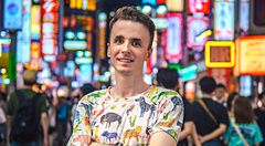 Marco Togni indossa una maglietta con disegni di animali a Shibuya davanti a insegne al neon luminose.