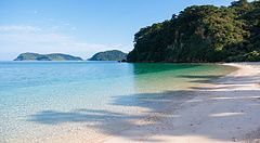 La spiaggia di Ida sull'isola di Iriomote presenta sabbia chiara e acque trasparenti vicino a un promontorio verde.