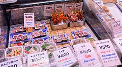 Spiedini di pesce crudo al mercato Nishiki di Kyoto con cartellini dei prezzi.