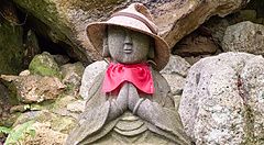 Statua di Jizo con cappello di paglia e bavaglio rosso tra le rocce.
